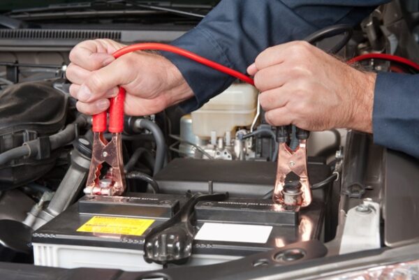 A car mechanic uses battery jumper cables to charge a dead battery.